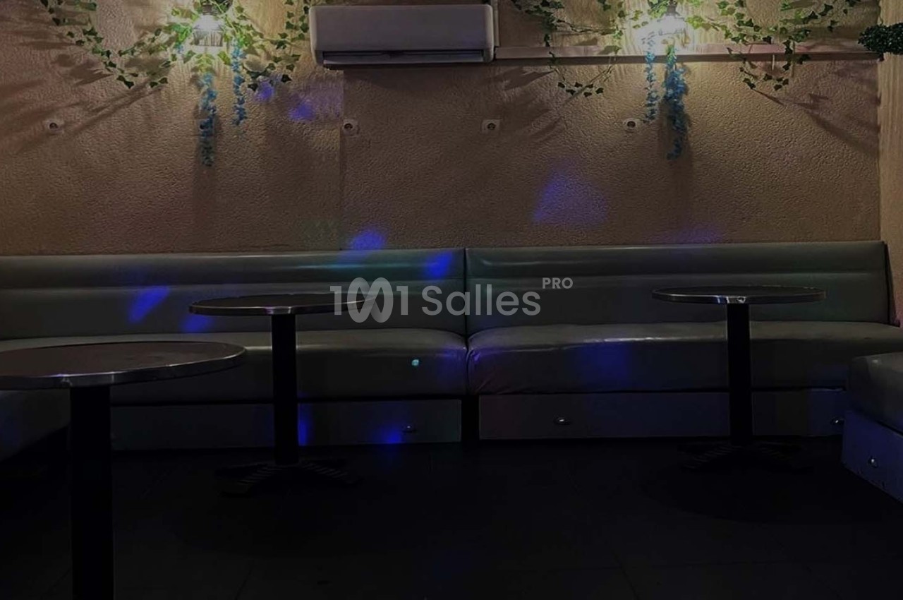 Banquettes grises et tables rondes dans une pièce sombre avec éclairage tamisé et décorations végétales murales.