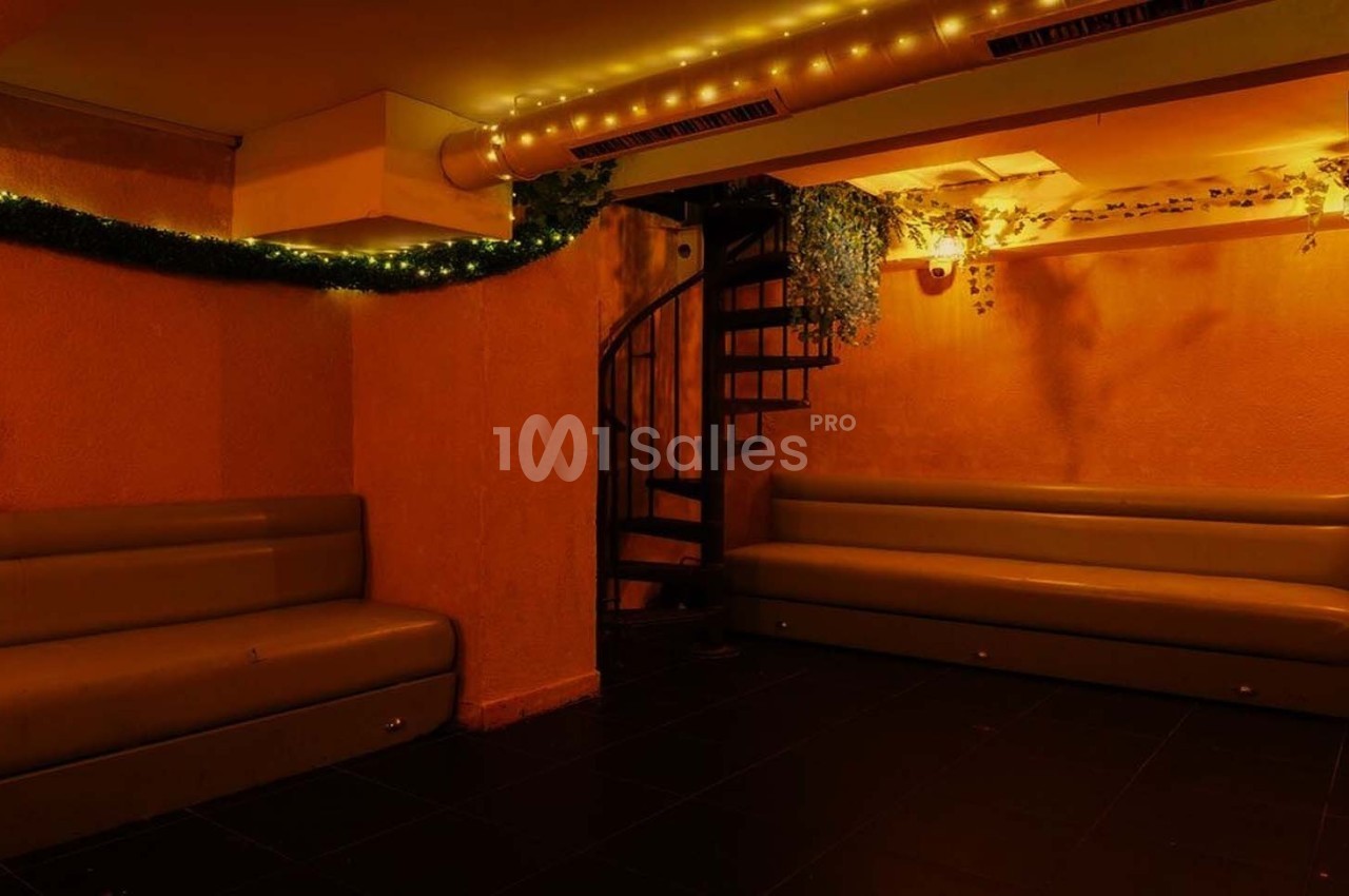 Salle avec des banquettes, un escalier en colimaçon, éclairage tamisé et décorations lumineuses et végétales.