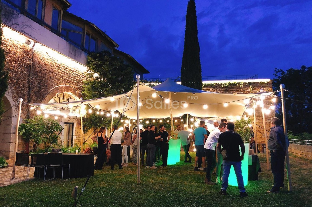 Groupe de personnes rassemblées sous un chapiteau éclairé par des guirlandes lumineuses dans un jardin en soirée.