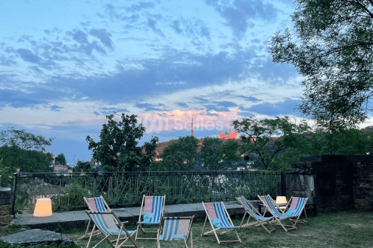 Chaises longues colorées disposées sur une pelouse au crépuscule, avec vue sur des arbres et un ciel nuageux.