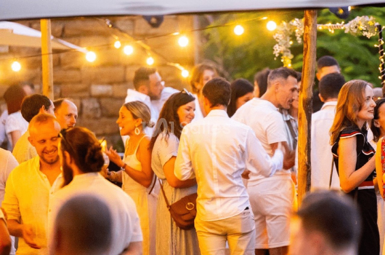 Groupe de personnes discutant et partageant un moment convivial lors d'un événement en extérieur, éclairé par des guirlandes…
