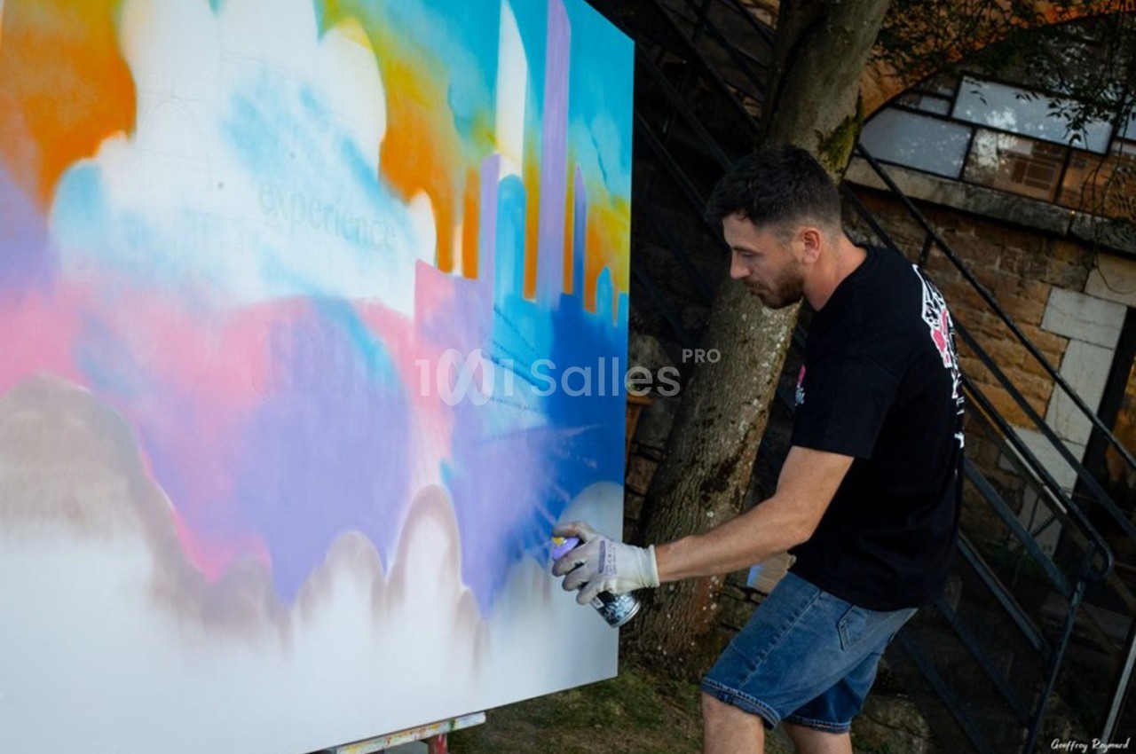 Un homme peint une fresque colorée à la bombe sur une grande toile en extérieur.