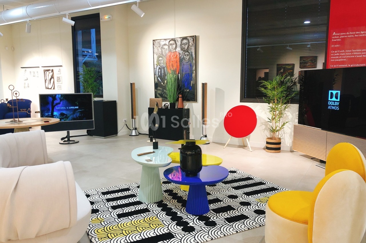 Salle d'exposition moderne avec mobilier design, œuvres d'art accrochées et équipements audiovisuels.