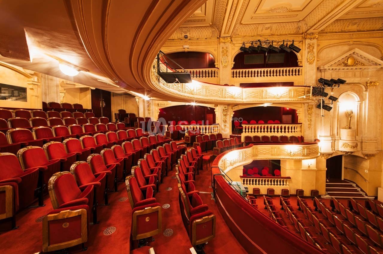Salle de théâtre avec des rangées de sièges rouges, balcons ornés et décorations architecturales élégantes.
