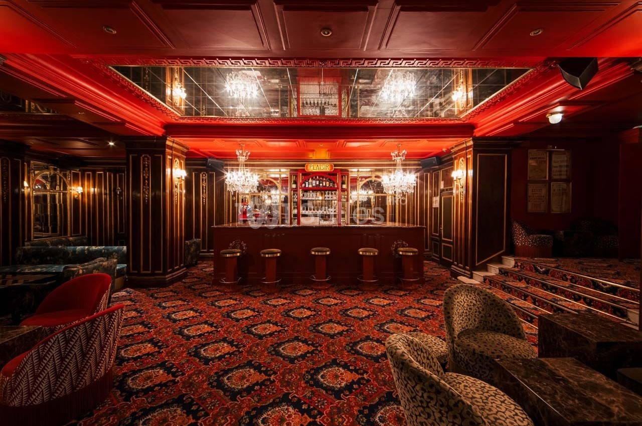 Intérieur d'un bar élégant avec comptoir central, tabourets, moquette ornée et éclairage chaleureux.