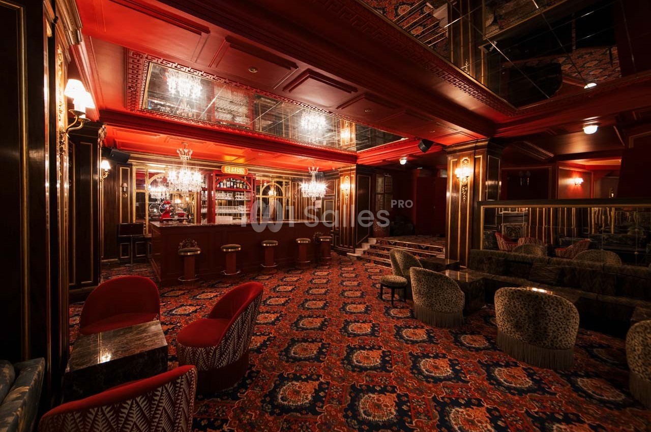 Salle de bar élégante avec moquette à motifs, fauteuils rembourrés, comptoir en bois et éclairage tamisé.