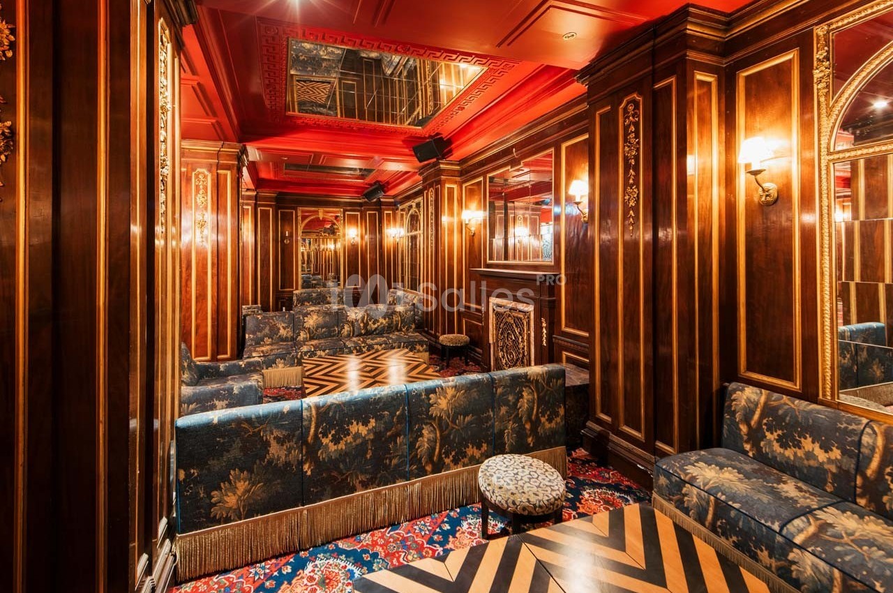 Salon élégant avec boiseries sombres, plafond rouge, miroirs, canapés fleuris et sol à motifs géométriques.