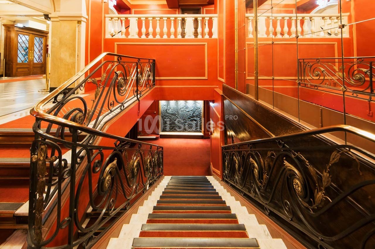 Escalier intérieur élégant avec rambardes en fer forgé, murs rouges et miroir reflétant l'espace.