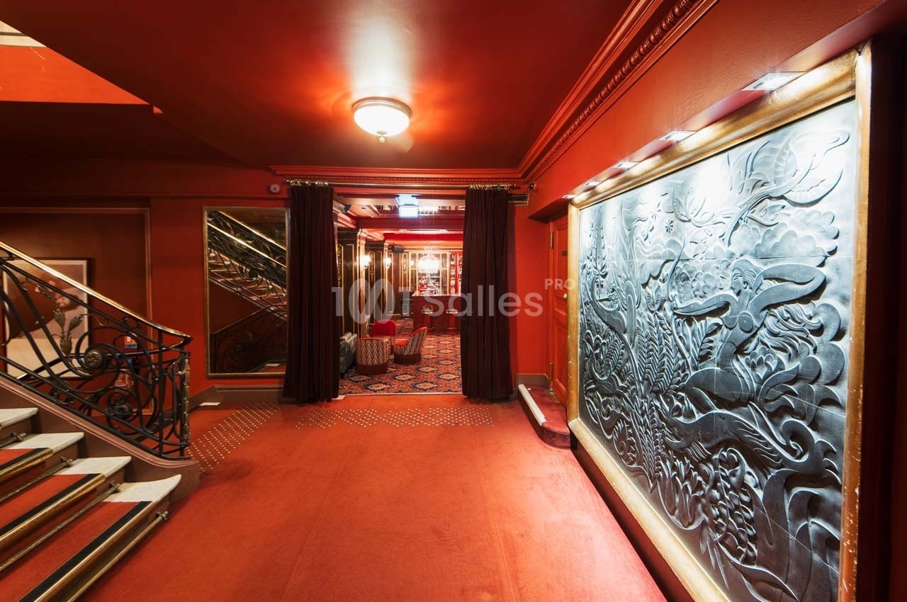 Escalier et couloir décoré de rouge avec fresque murale sculptée, éclairage chaleureux et moquette au sol.