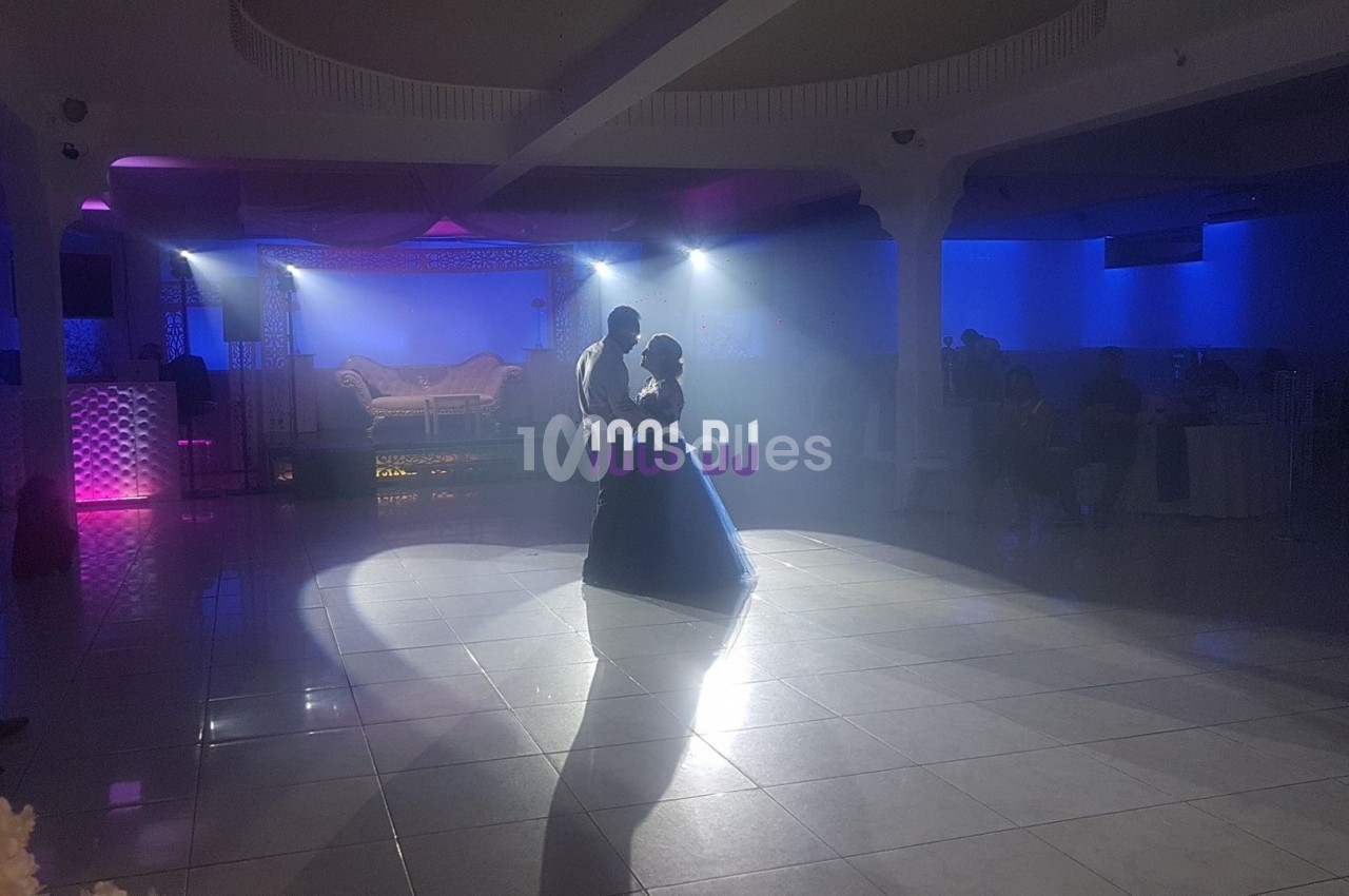 Un couple danse sous des projecteurs dans une salle de réception éclairée par des lumières colorées.