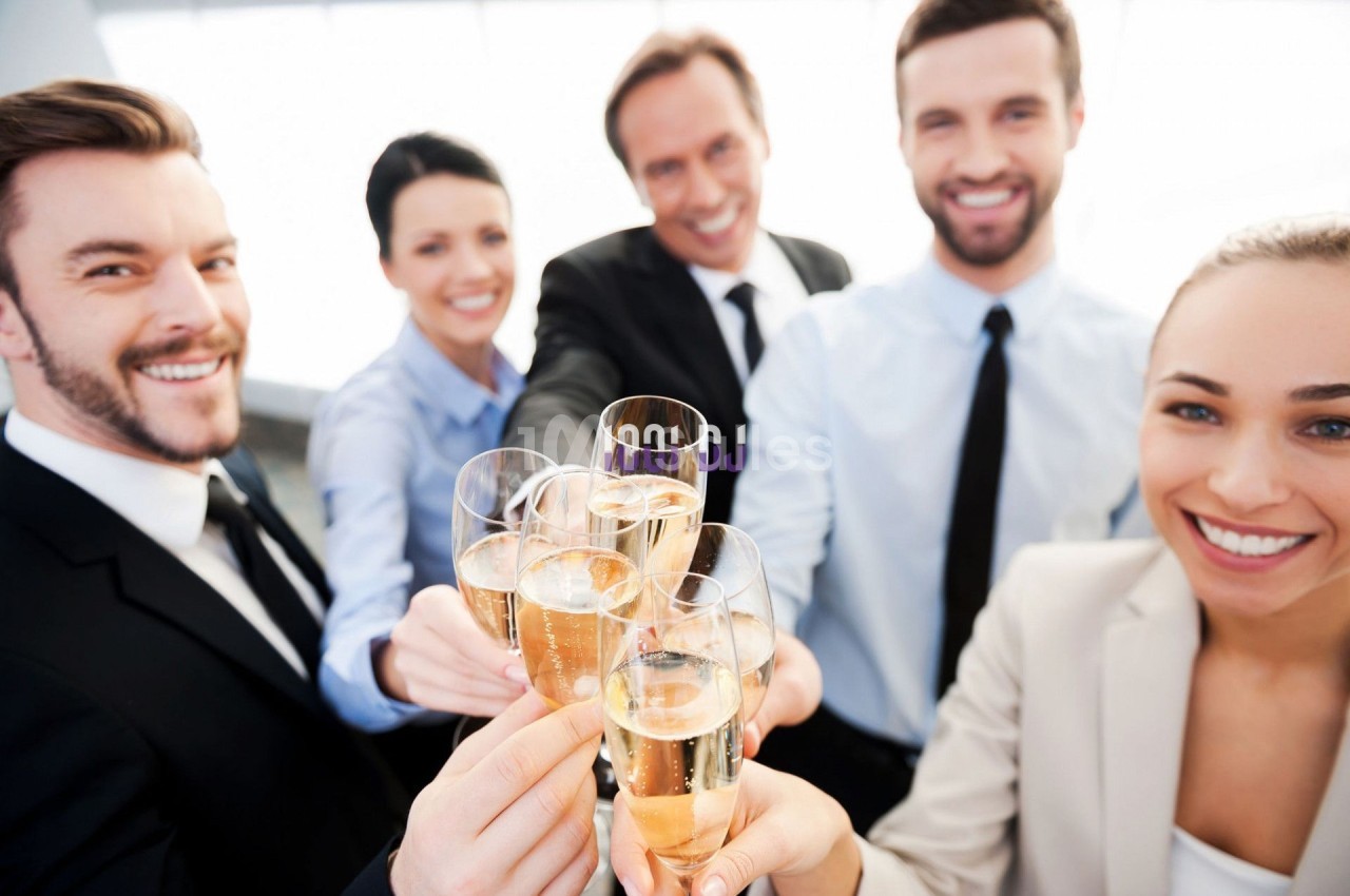 Des collègues souriants trinquent avec des verres de champagne dans un cadre professionnel lumineux.