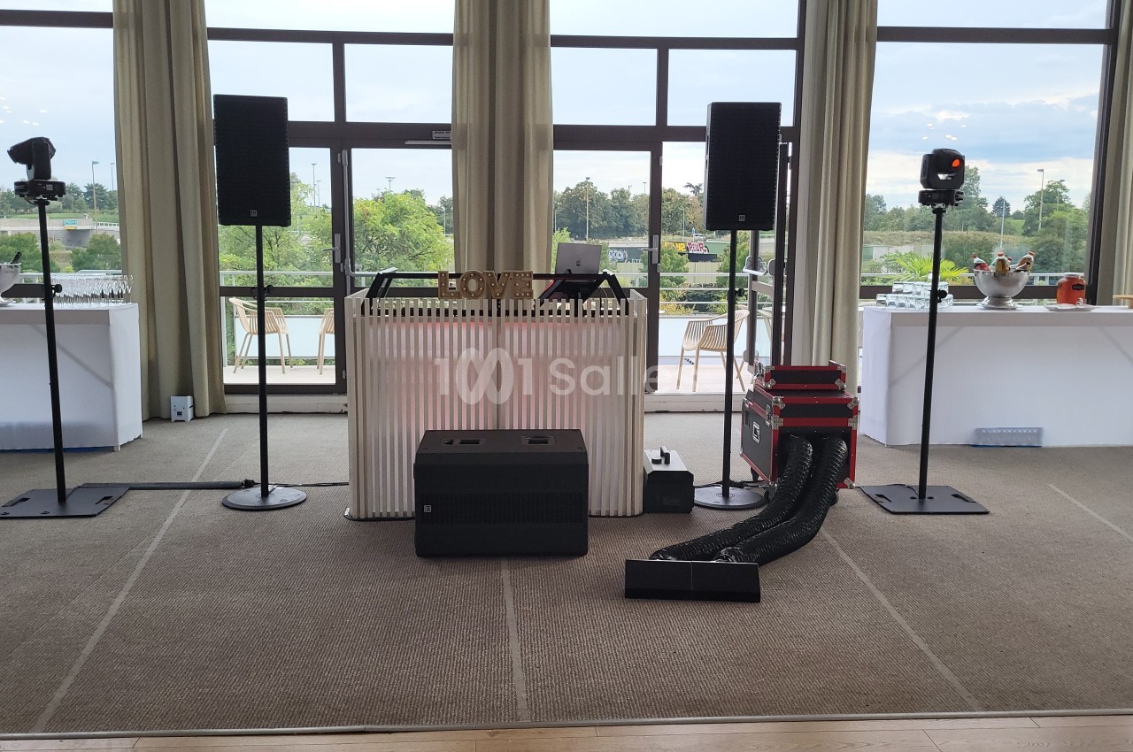 Installation de matériel audio avec enceintes, table de mixage et éclairage dans une salle avec grandes baies vitrées.