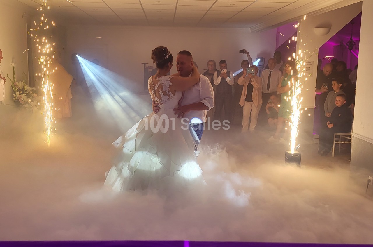 Un couple danse au milieu d'une salle décorée avec des effets de fumée et des étincelles, entouré d'invités.