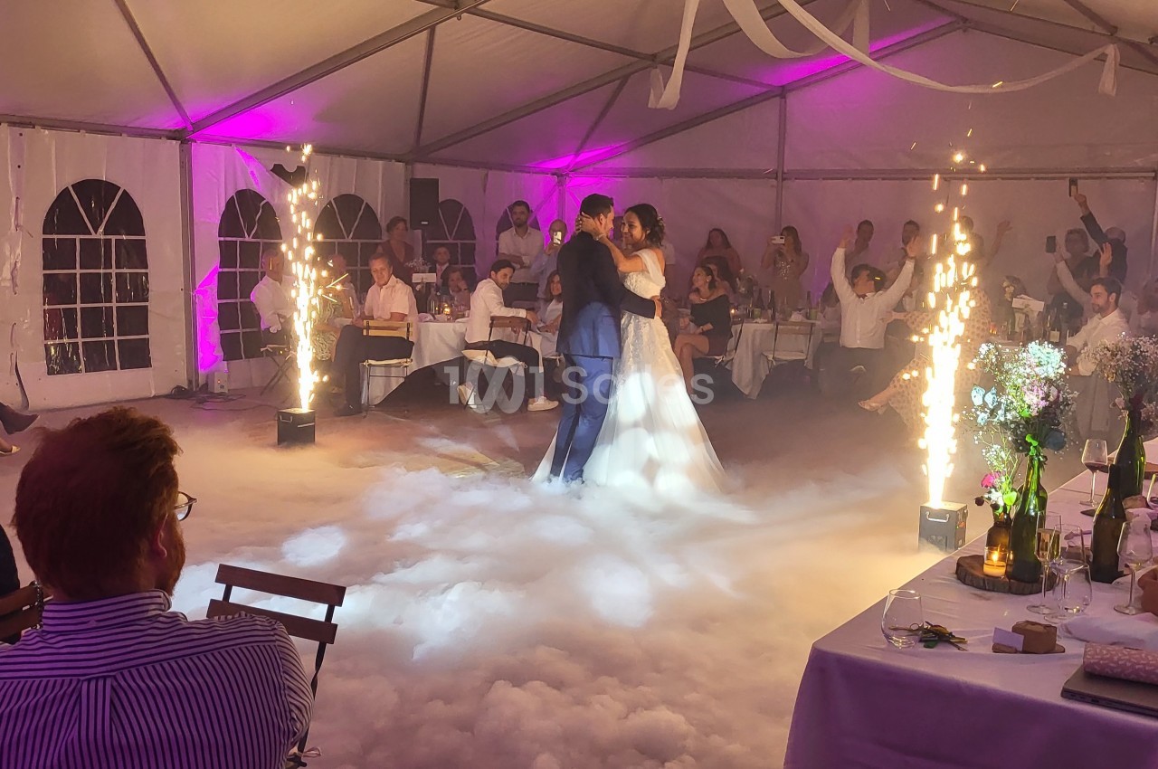 Un couple danse au milieu d'une piste entourée de fumée et d'étincelles dans une salle décorée pour un événement.