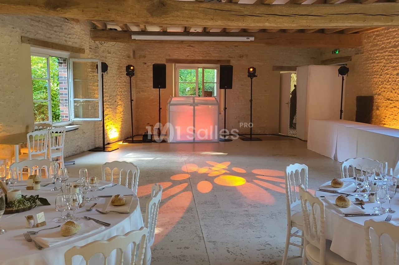 Salle de réception en pierre avec tables dressées, éclairage chaleureux et espace dédié à un DJ.