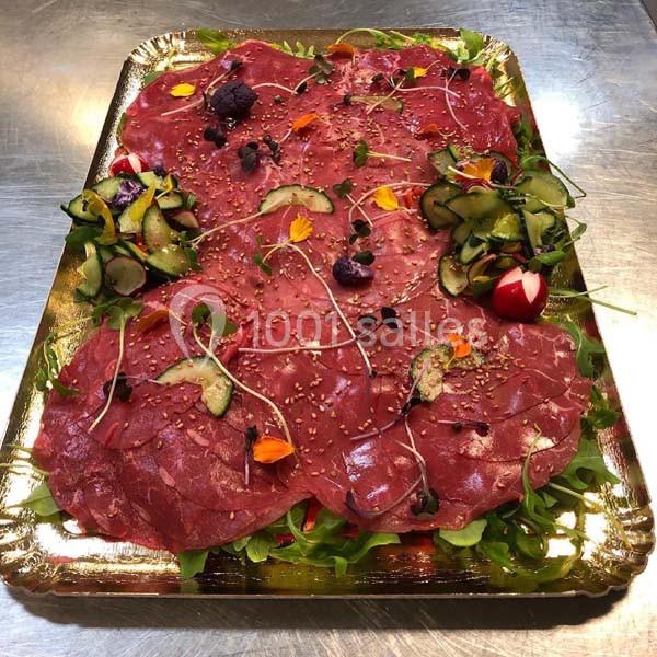 Plateau de carpaccio de bœuf garni de roquette, légumes frais, graines de sésame et fleurs comestibles.