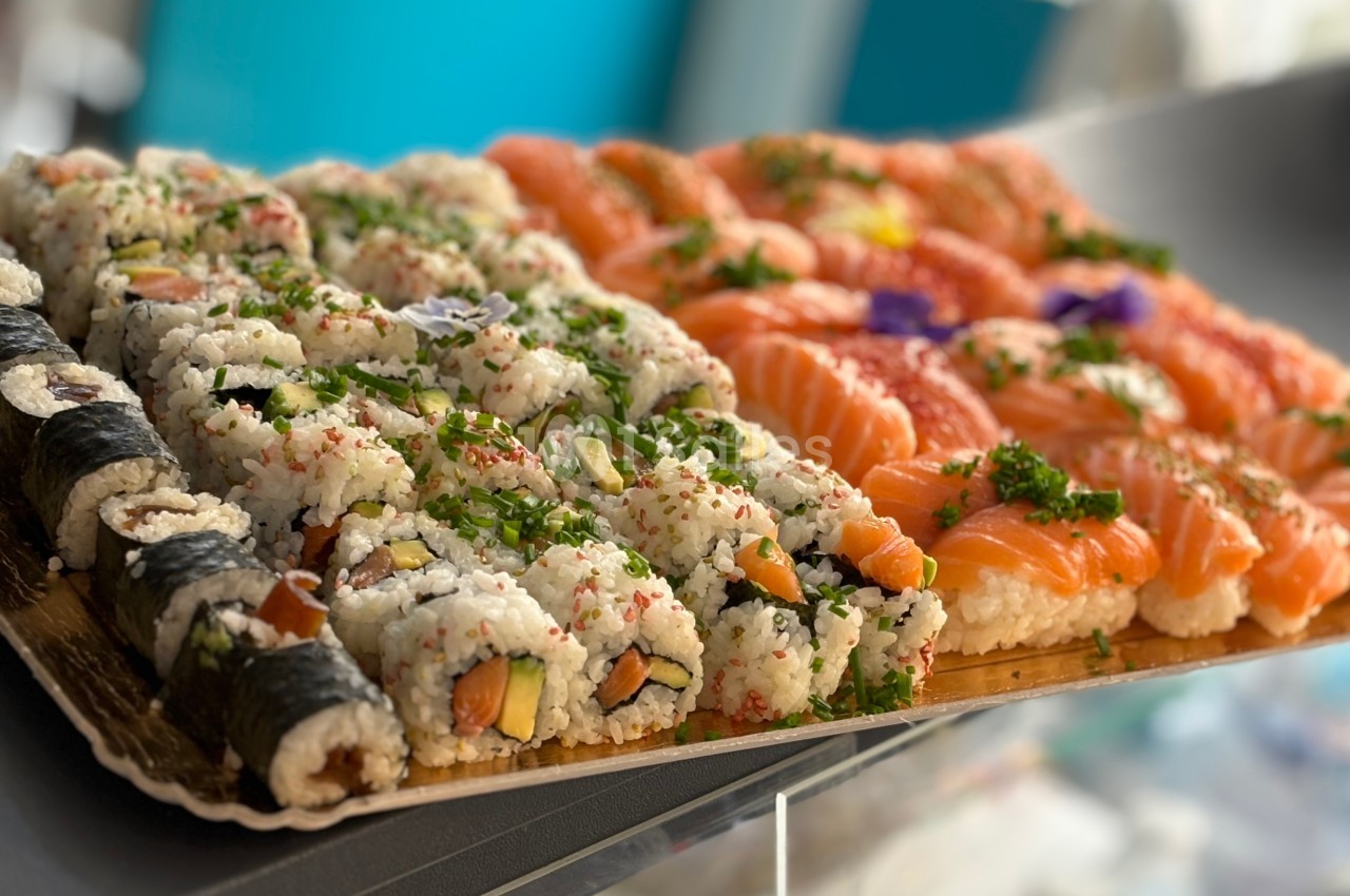 Plateau de sushis variés comprenant des makis, des california rolls et des sashimis au saumon, présenté sur un comptoir.
