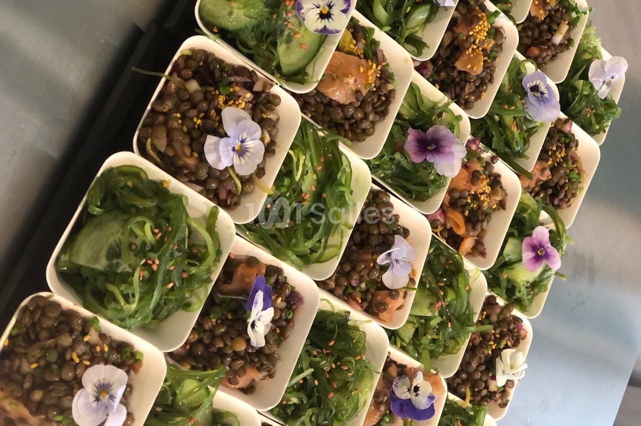 Assortiment de verrines garnies de lentilles, algues, saumon et fleurs comestibles, disposées sur un plateau.