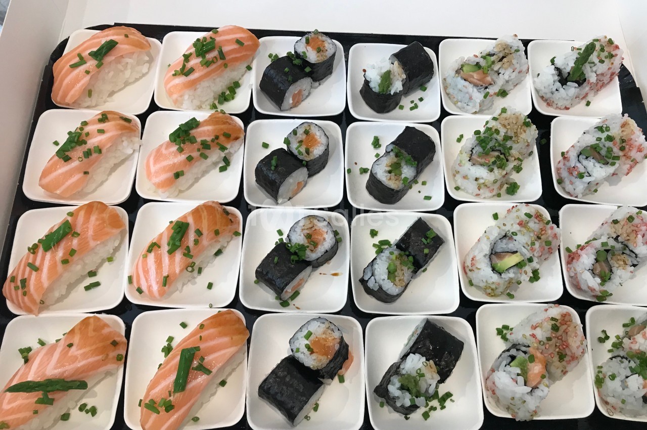 Plateau de sushis variés disposés sur des assiettes individuelles, comprenant nigiris au saumon et makis garnis.