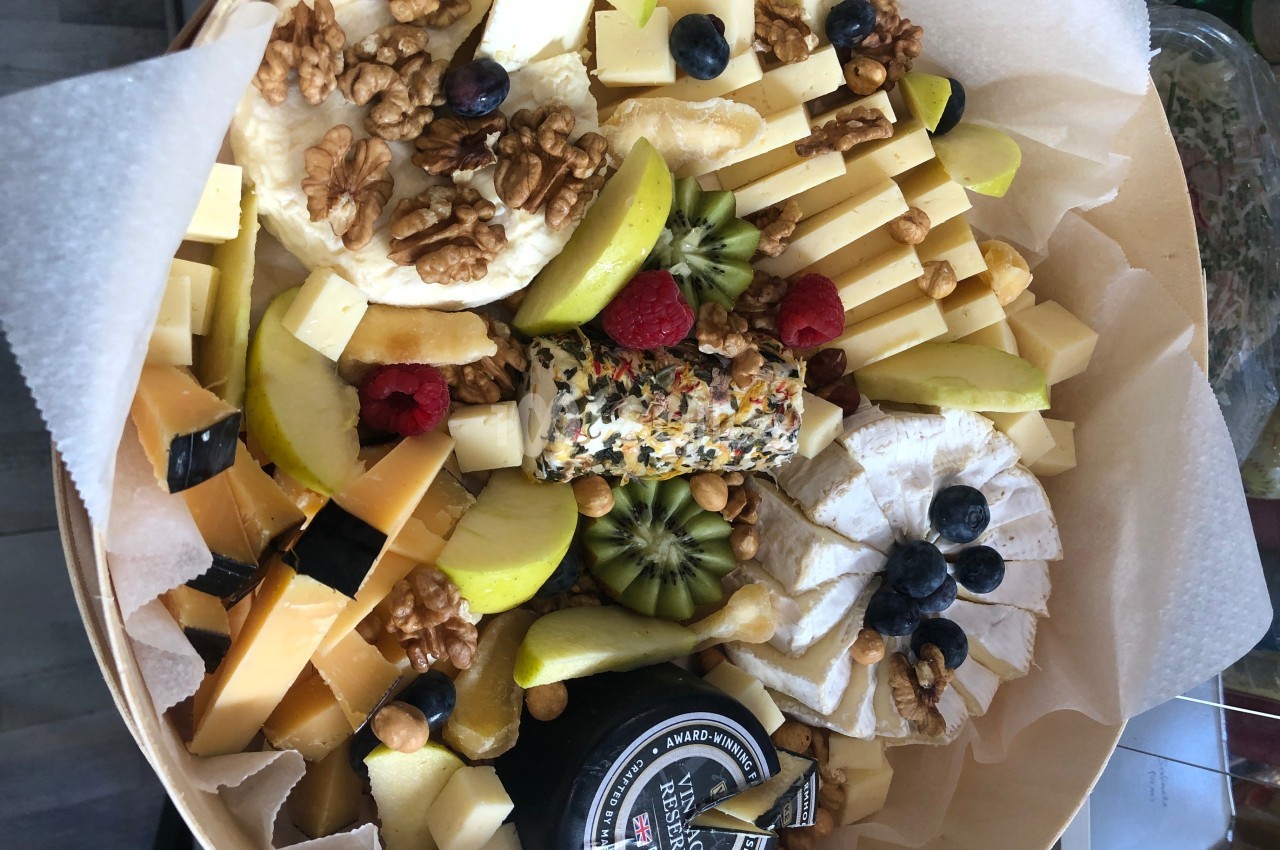 Plateau garni de fromages variés, fruits frais, noix et un fromage roulé aux herbes, présenté sur du papier parchemin.