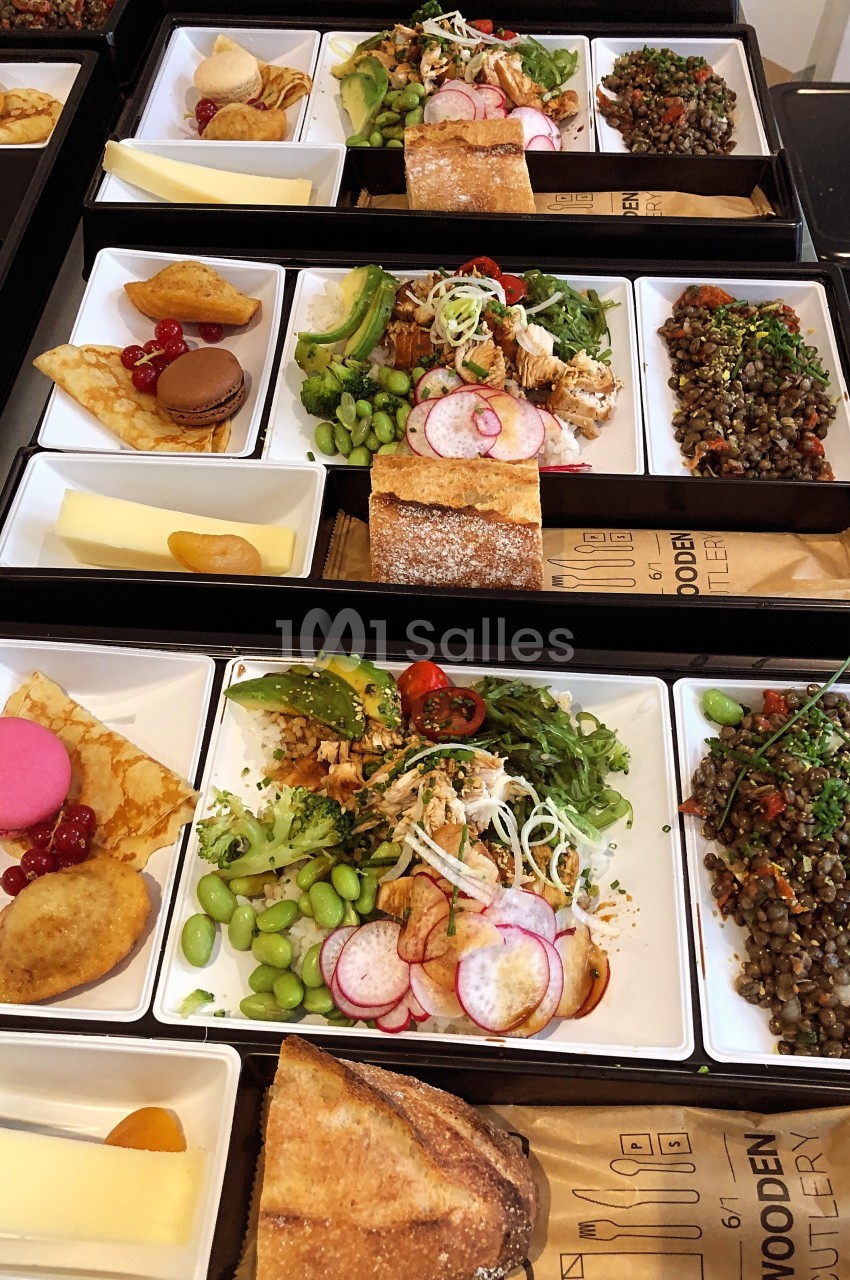 Plateaux-repas variés comprenant salade, lentilles, fromage, pain, pâtisseries et fruits, disposés sur une table.