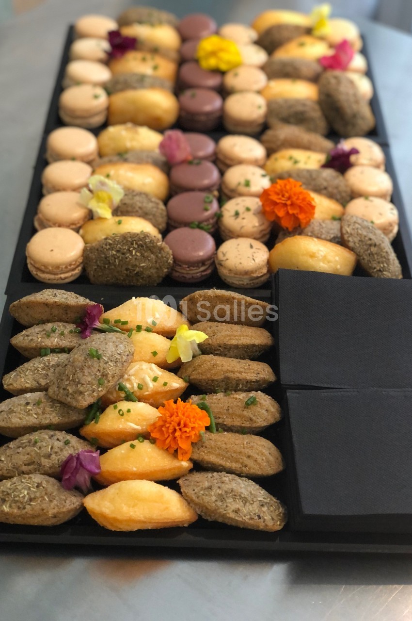 Plateau de mignardises variées comprenant macarons, madeleines et bouchées salées, décoré de fleurs comestibles.