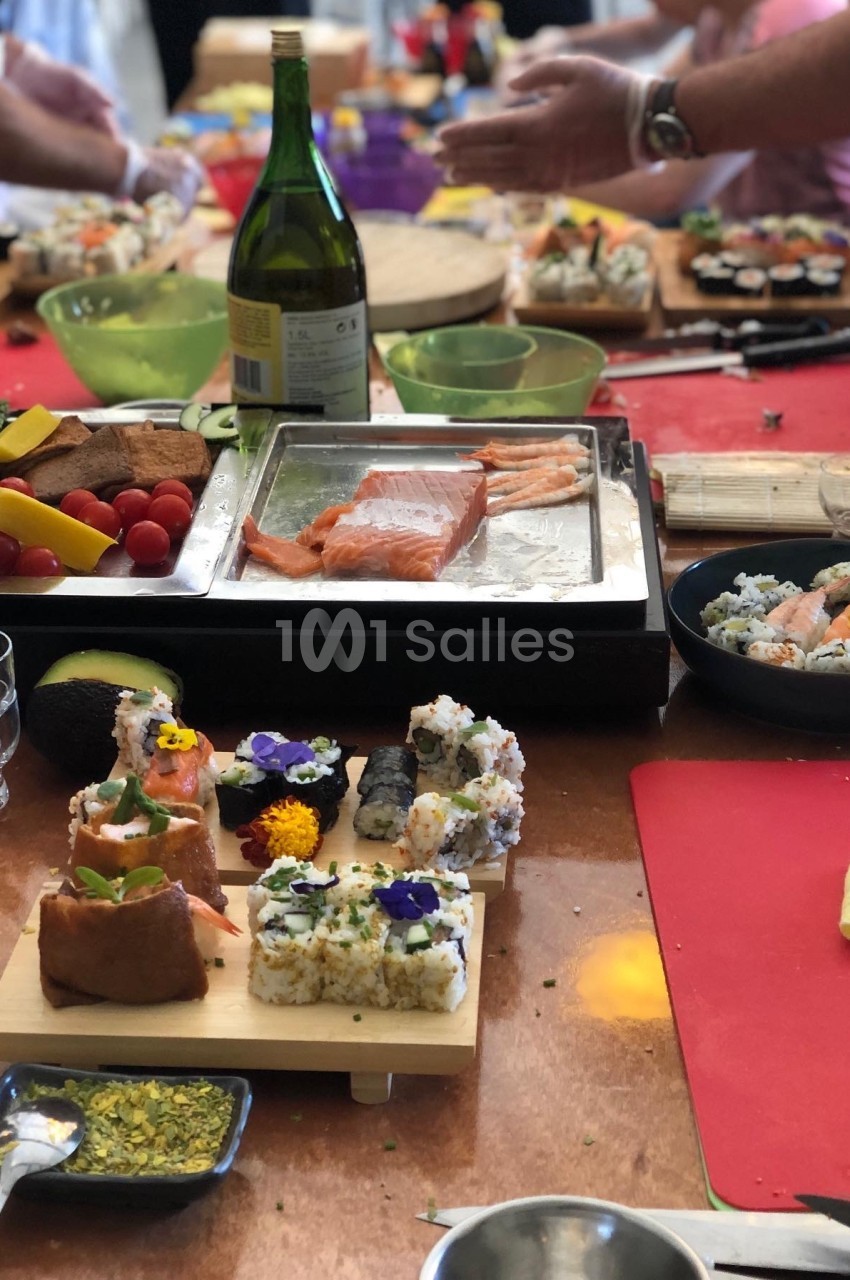 Atelier culinaire avec préparation de sushis et makis, ingrédients frais et ustensiles disposés sur une table.
