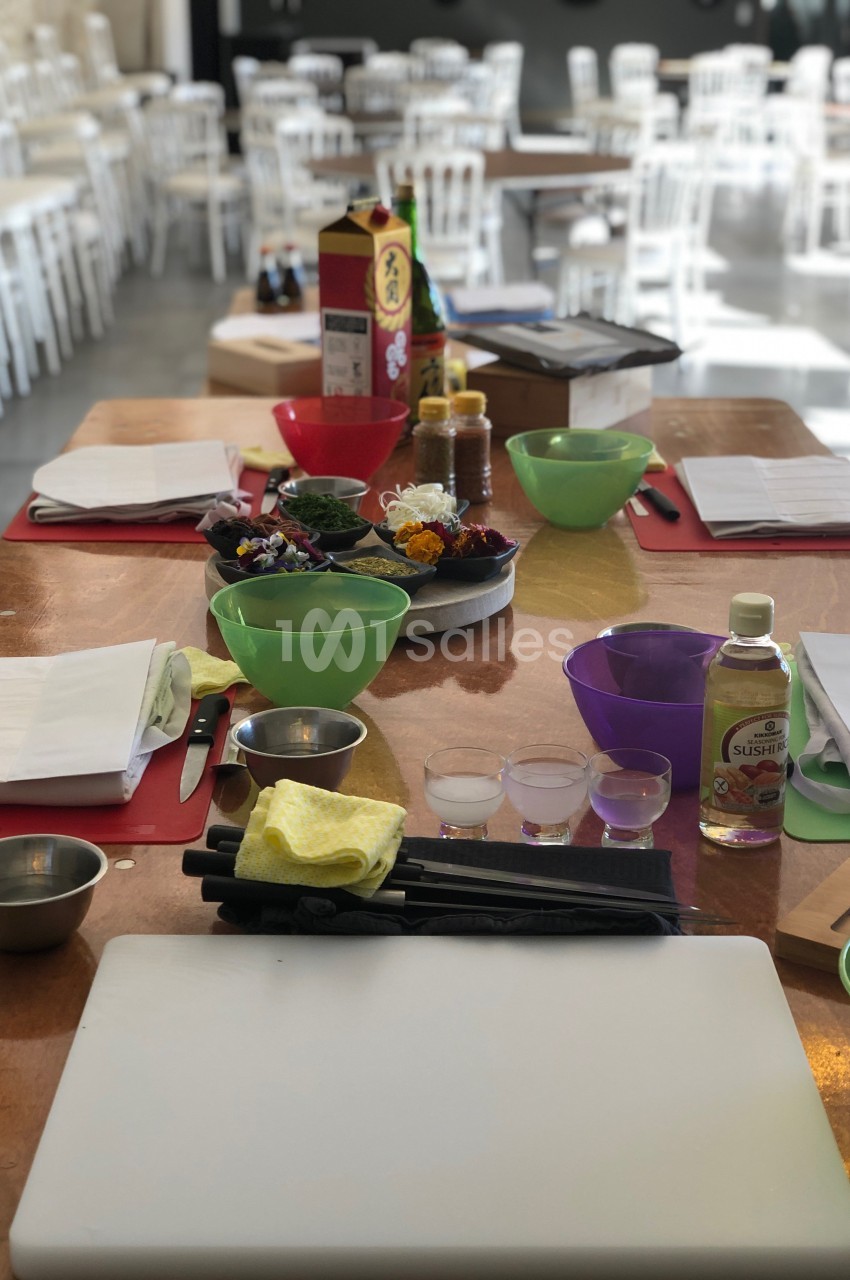 Plan de travail avec ustensiles de cuisine, planches à découper, bols et ingrédients, dans une salle lumineuse.