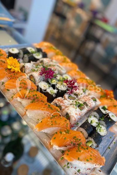 Plateau de sushis variés avec makis, nigiris au saumon et garnitures de fleurs comestibles et ciboulette.