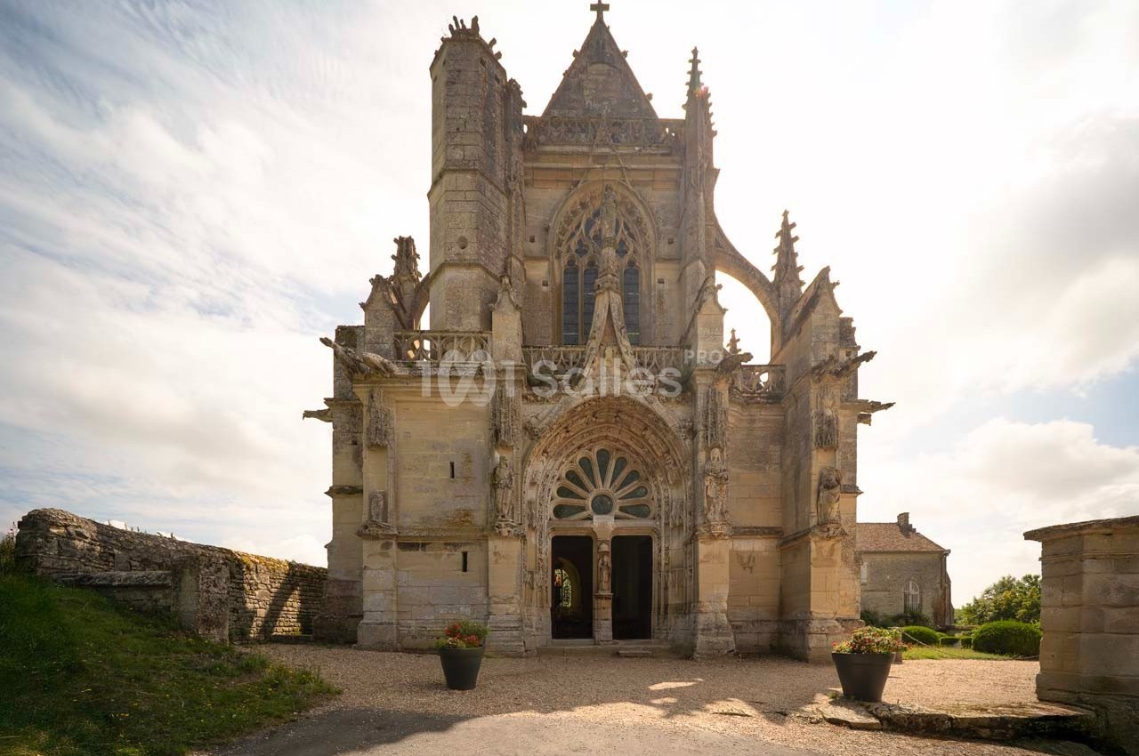 Façade d'une petite église gothique avec des détails sculptés, entourée de végétation et baignée de lumière naturelle.