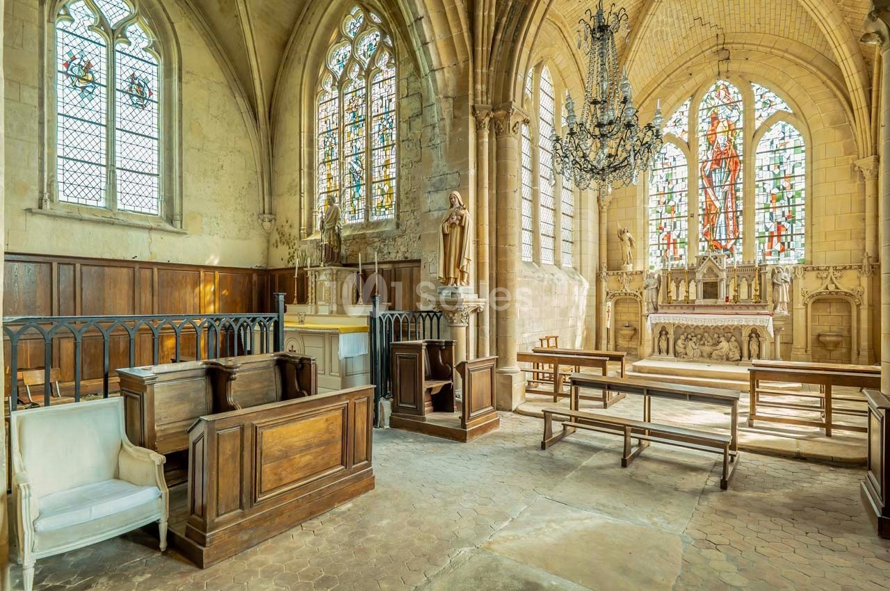Intérieur d'une église avec autel, vitraux colorés, statues religieuses et bancs en bois sous un lustre suspendu.