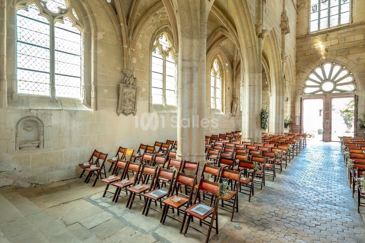 Intérieur d'une église avec des rangées de chaises en bois alignées sous des voûtes et des fenêtres gothiques.