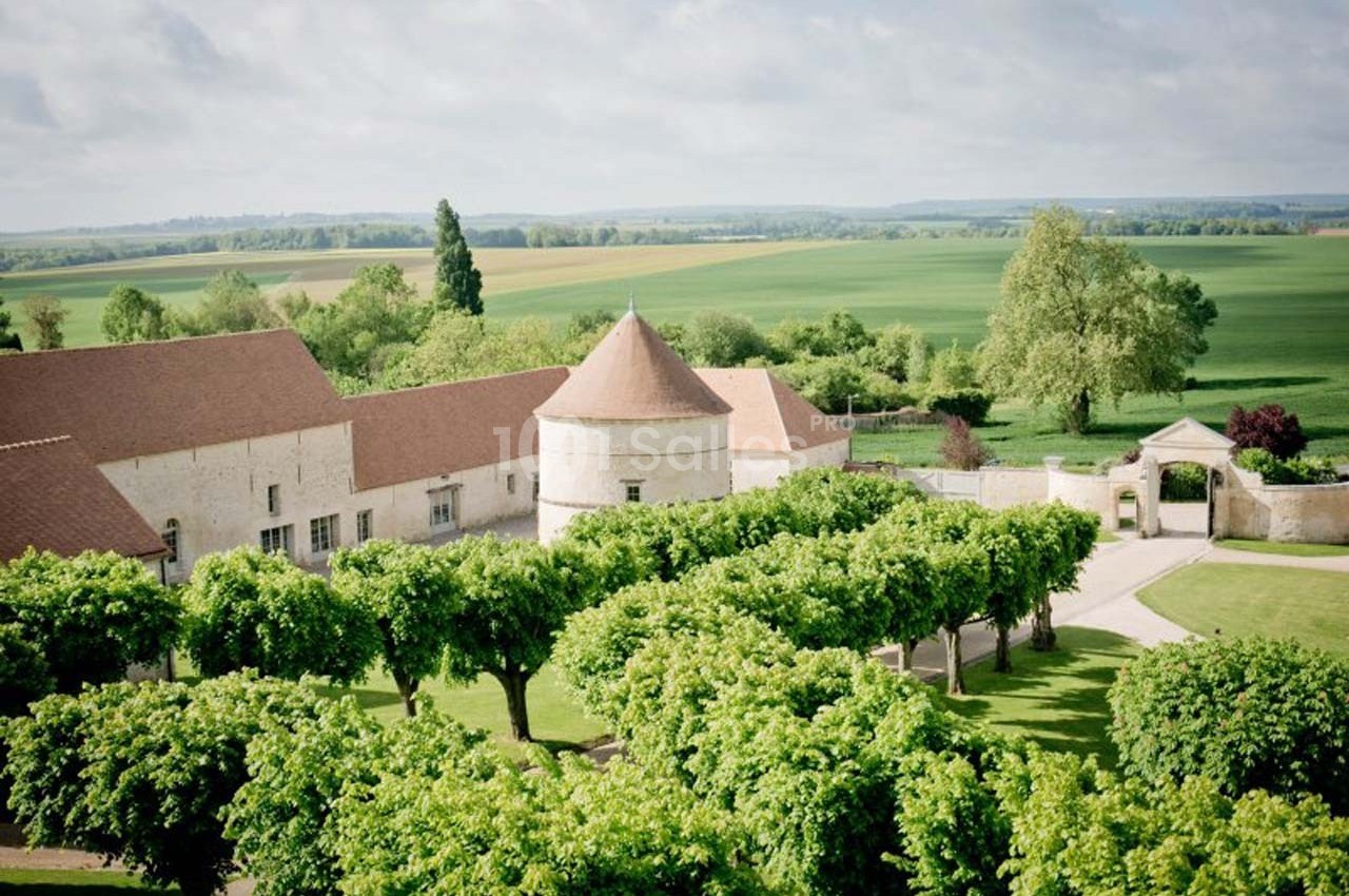 Vue aérienne d'un domaine rural avec bâtiments en pierre, toits rouges, allée bordée d'arbres et champs verdoyants en…