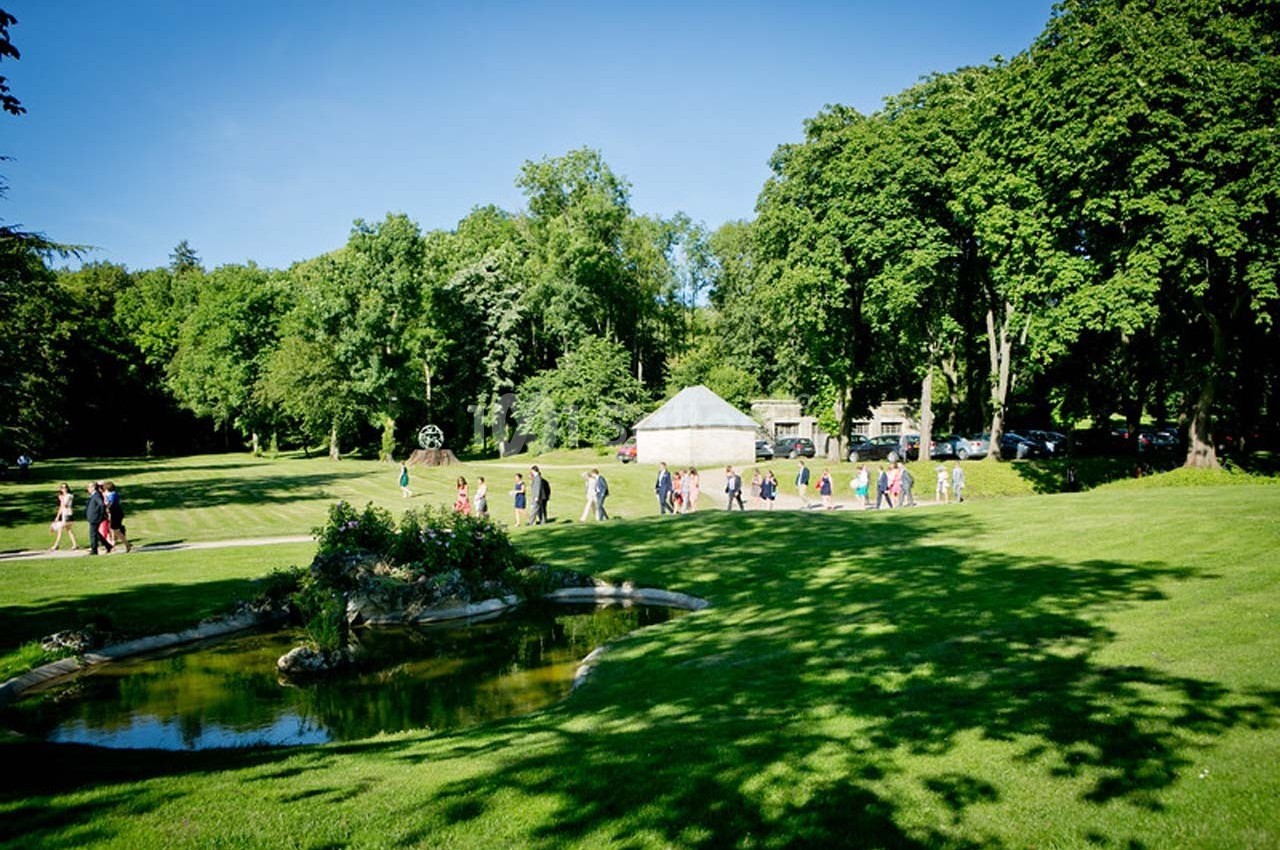 Un groupe de personnes marche dans un parc verdoyant avec une petite mare au premier plan et des arbres en arrière-plan.