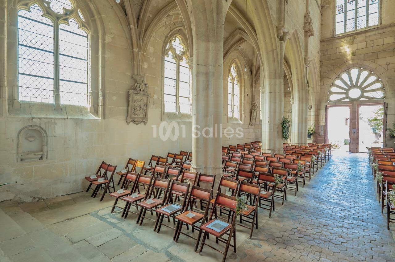 Intérieur d'une église avec des rangées de chaises en bois alignées sous des voûtes et des vitraux.