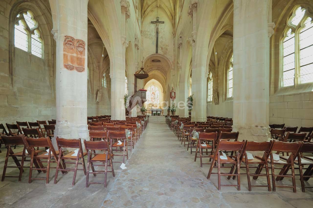 Intérieur d'une église avec des rangées de chaises en bois, un autel décoré et des vitraux laissant entrer la lumière.