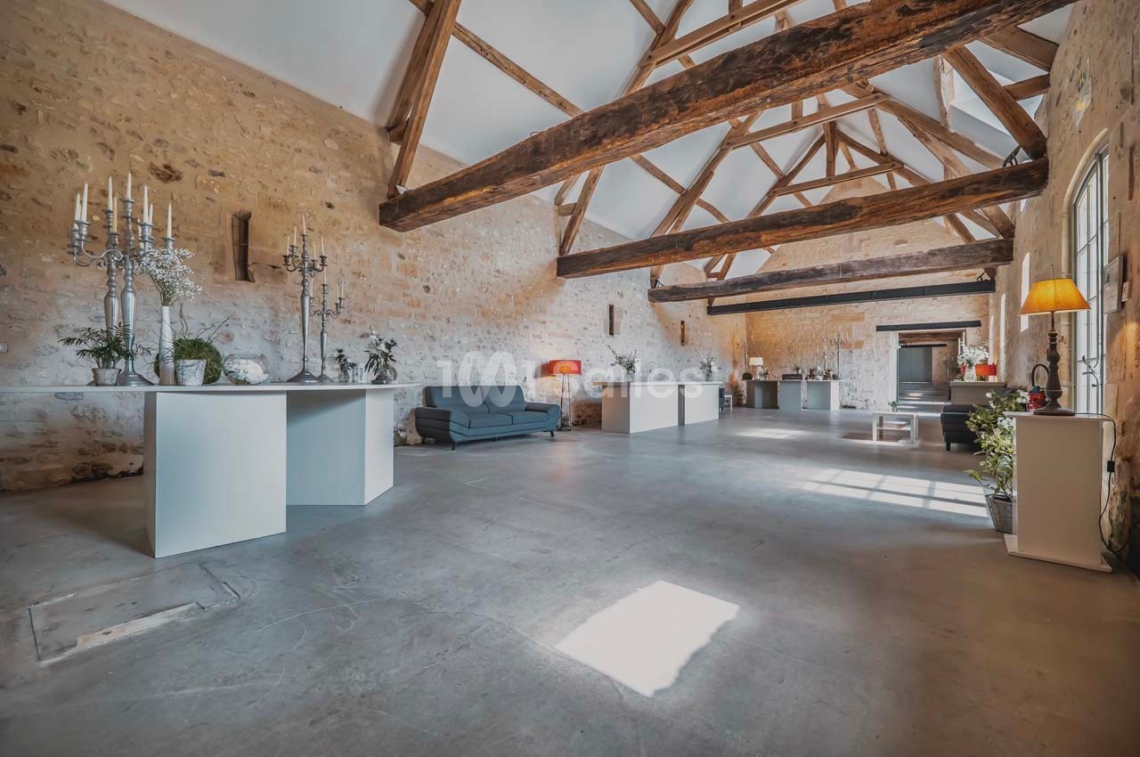 Salle spacieuse avec murs en pierre, poutres apparentes, mobilier moderne et lumière naturelle entrant par les fenêtres.