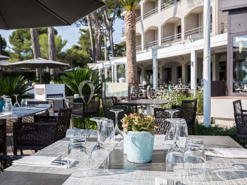 Terrasse d'un restaurant avec tables dressées, entourée de végétation et située devant un bâtiment moderne.