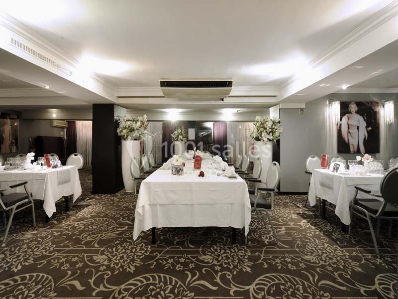 Salle de réception élégante avec tables dressées, nappes blanches, chaises grises et décorations florales.