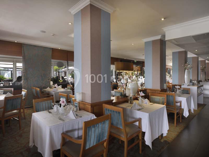 Salle de restaurant élégante avec tables dressées, nappes blanches, chaises en bois et décoration florale.