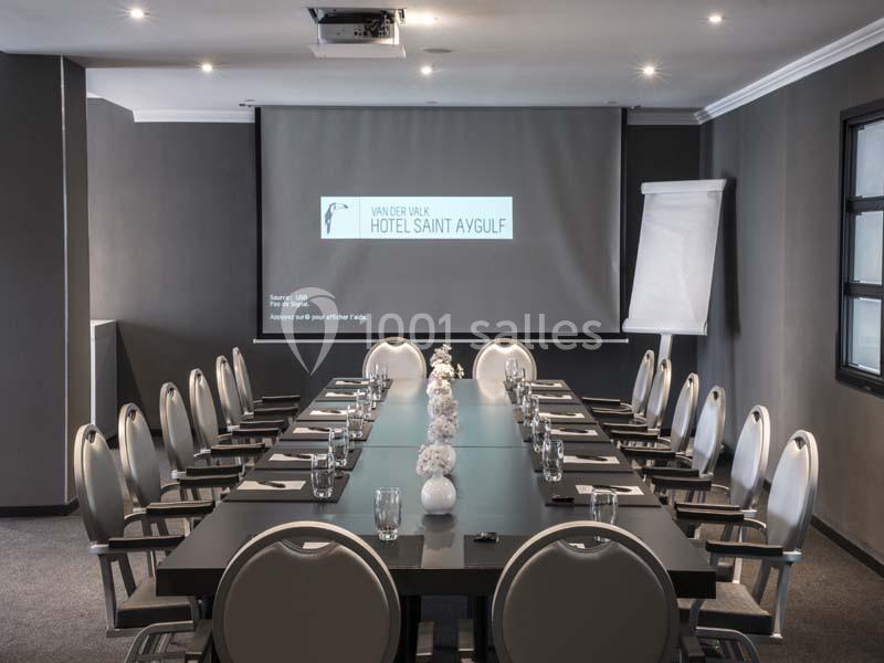 Salle de réunion moderne avec une grande table, des chaises, un écran de projection et un paperboard.