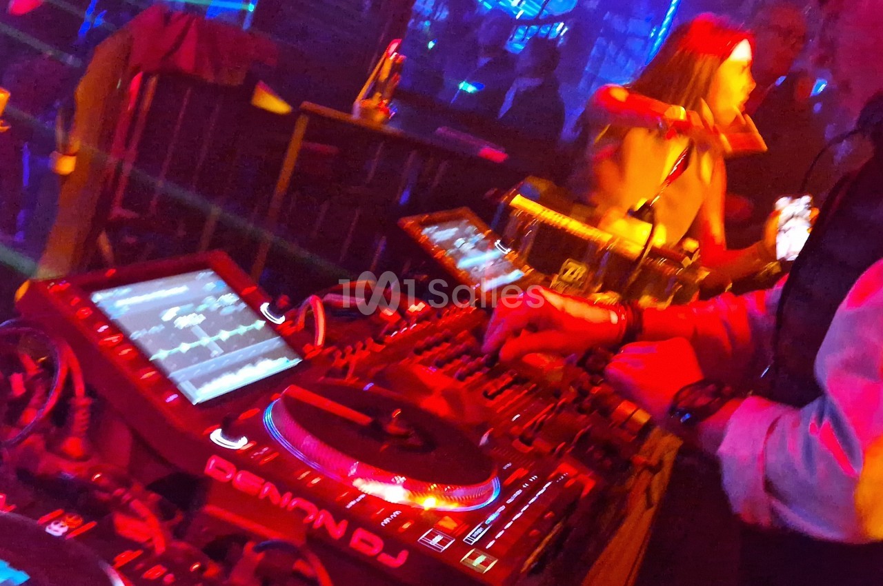 Un DJ mixe de la musique sur une console lumineuse dans une ambiance de boîte de nuit colorée.