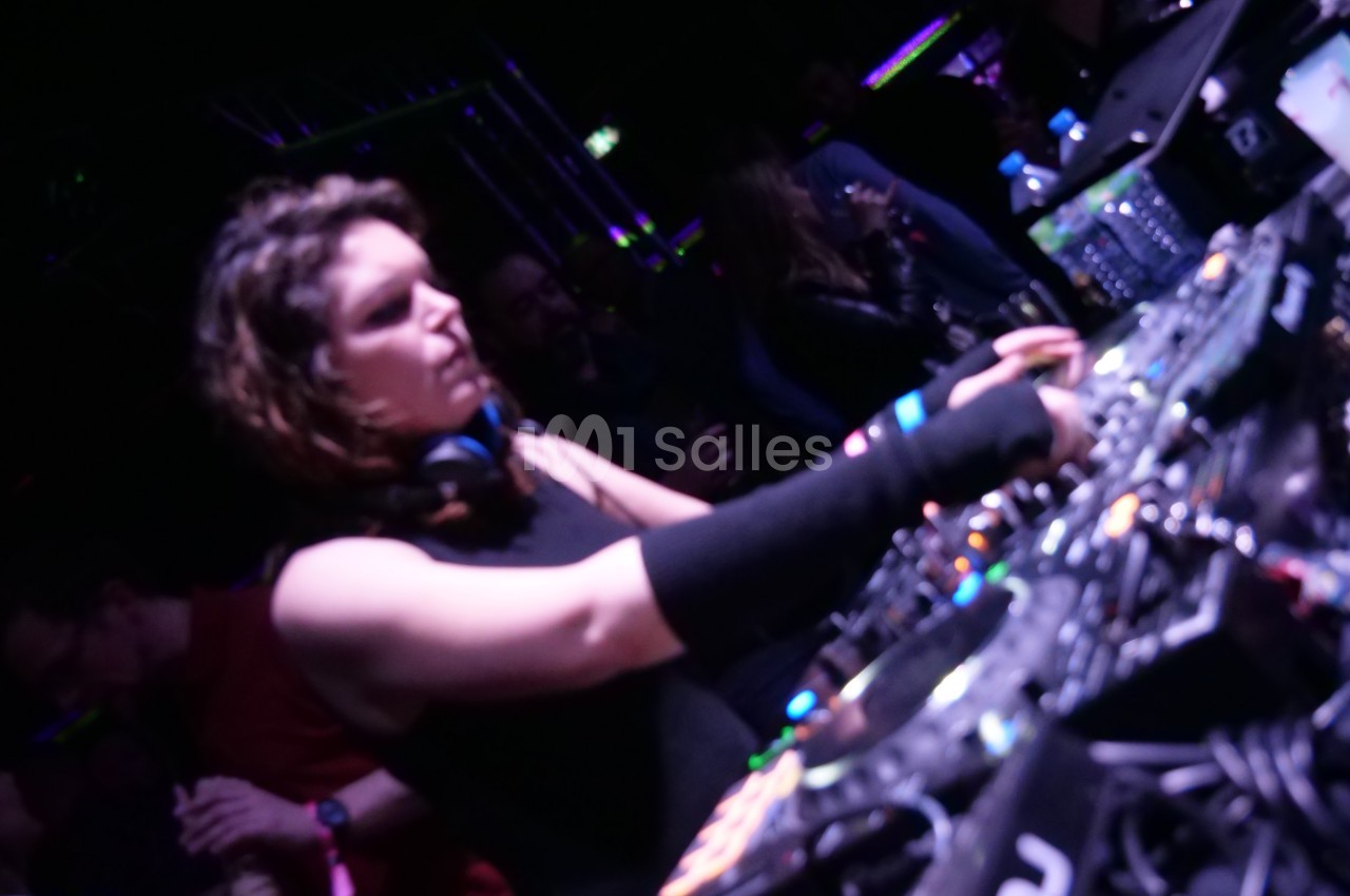 Une DJ mixe de la musique sur une table de mixage dans une ambiance sombre avec des lumières colorées.