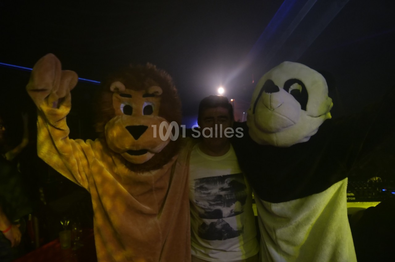 Un homme pose entre deux personnes déguisées en lion et en panda dans un environnement sombre avec des lumières.