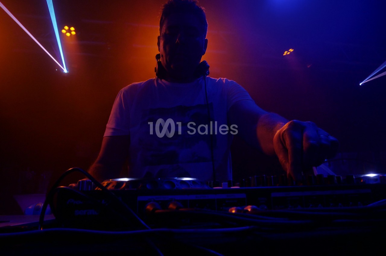 Un DJ mixant sur une console dans une ambiance lumineuse rouge et bleue lors d'une performance en soirée.