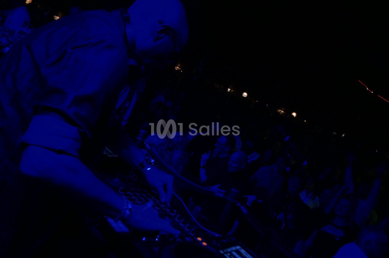 Un DJ mixant sur une table de mixage dans une ambiance sombre, entouré d'un public en arrière-plan.