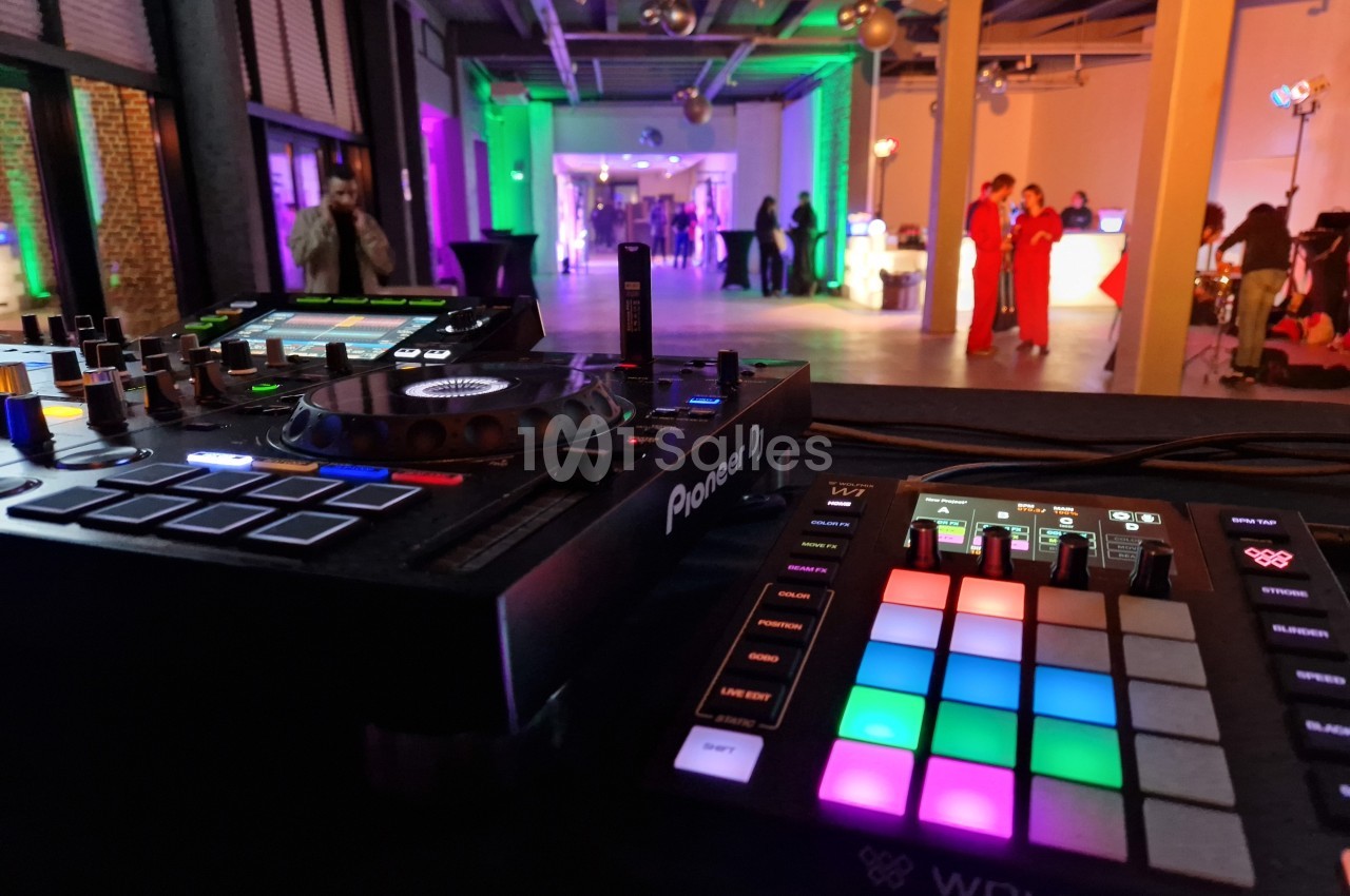 Vue rapprochée d'une console DJ et d'un contrôleur lumineux, avec une salle éclairée en arrière-plan.