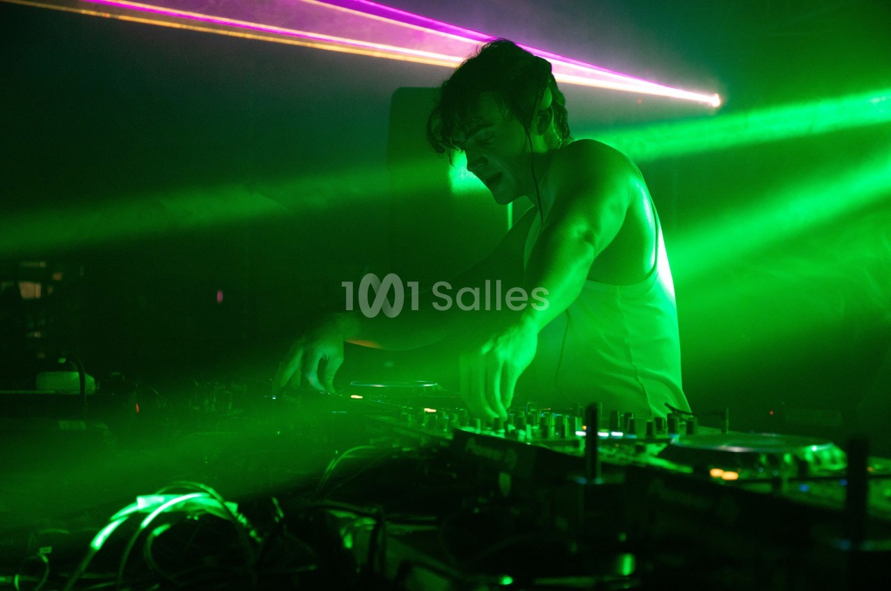 Un DJ mixe de la musique sur une table de mixage dans une ambiance lumineuse verte avec des faisceaux laser.