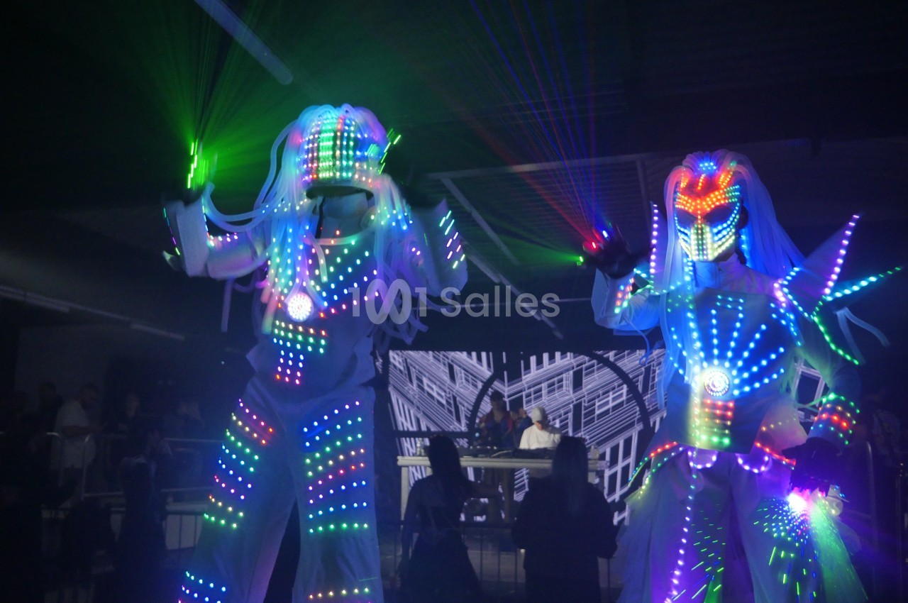 Deux personnes en costumes lumineux LED multicolores dans un environnement sombre avec des faisceaux laser.