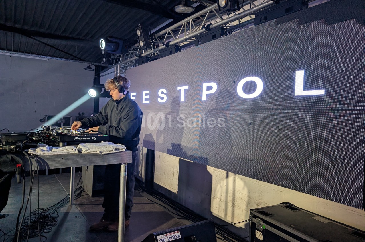 Un DJ mixe sur une scène éclairée devant un écran affichant le mot ’ESTPOL’.